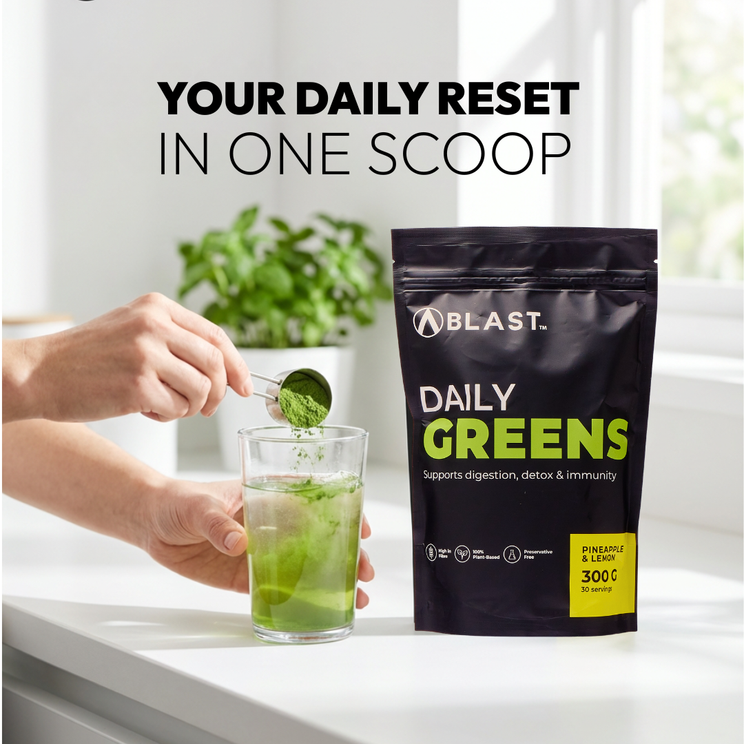 Person adding green powder to a glass with a 'Blast Daily Greens' package on a white surface.