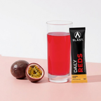 Blast Daily Red juice in a glass with a Blast Daily Reds supplement on a pink background